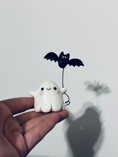 a hand holding a tiny white ghost with a bat on it's back and the shadow of a plant behind it