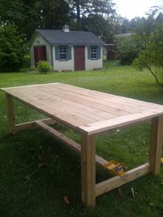 a wooden table sitting on top of a lush green field next to a small house