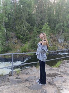 a woman standing on top of a rock covered hillside next to a river and forest