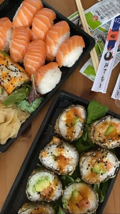 two trays filled with sushi and other food on top of a wooden table