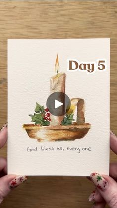 someone holding up a card with a candle and holly wreath on it, which reads day 5