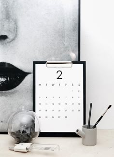 a calendar with the number two on it next to a cup and pencils in front of a photograph