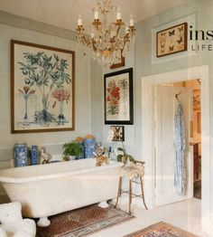 a white bath tub sitting under a chandelier next to a doorway with pictures on the wall