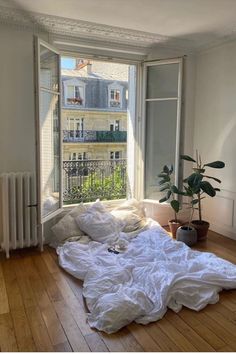 an unmade bed sitting in front of a window on top of a hard wood floor