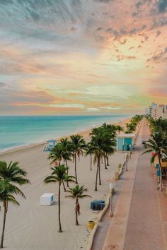 the beach is lined with palm trees as the sun sets over the ocean and buildings