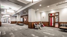 two people are sitting in the waiting area of a large building with wood paneling