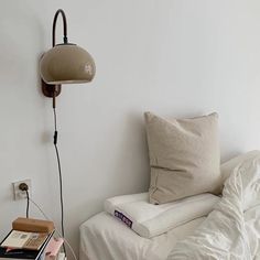 a bed with white sheets and pillows next to a lamp on the wall above it