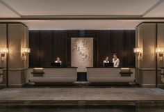 two people are sitting at the front desk of a hotel lobby with marble walls and flooring