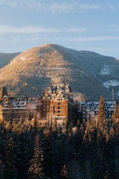 a large building surrounded by trees in front of a mountain with snow on the top