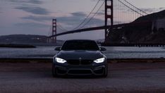 a black car is parked in front of the golden gate bridge at night with its lights on