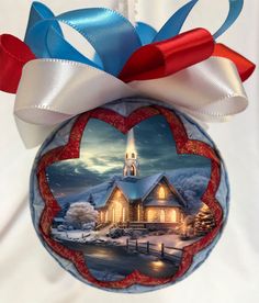 a christmas ornament with a church in the background and a red white and blue ribbon