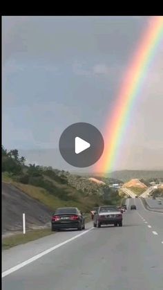 a rainbow is seen in the sky over cars driving down a road with hills and trees