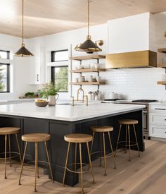 a kitchen with black and white cabinets, gold accents and stools on the island