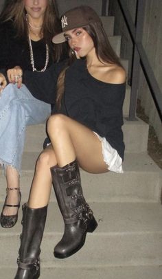 two young women sitting on the steps with their legs crossed and one is wearing boots