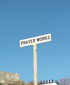 a white street sign sitting on top of a metal pole under a blue sky with mountains in the background