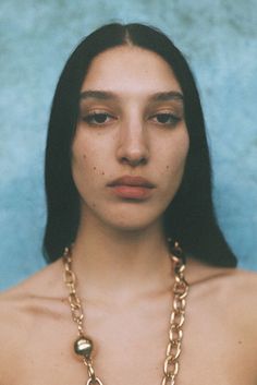 a woman with long black hair wearing a gold chain around her neck is looking at the camera