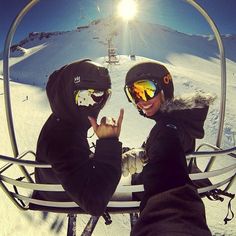 two people in ski gear sitting on a chair lift giving the peace sign with their hands