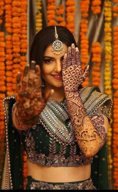 a woman in a green and gold outfit holding her hands up to her face with hendi