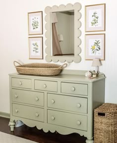 a dresser with a basket on top of it in front of a mirror and pictures