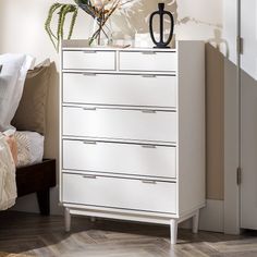 a white chest of drawers sitting next to a bed with flowers on top of it