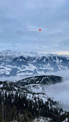 the mountains are covered in snow and clouds with a red balloon flying above them on a cloudy day