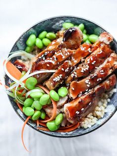 a bowl filled with meat and vegetables on top of rice covered in sesame seed sauce