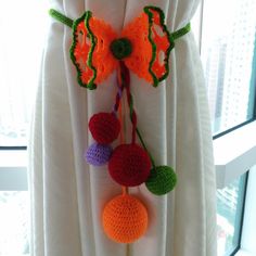 an orange and green crochet decoration hanging from a curtain with pom - poms