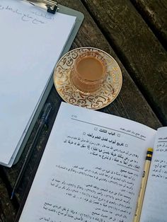 an open book with arabic writing on it next to a cup of coffee and a pencil