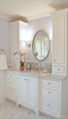 a large bathroom with white cabinets and marble counter tops, along with a round mirror on the wall