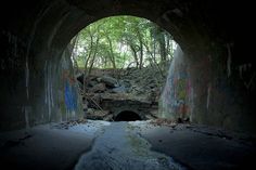 a dark tunnel with graffiti on the walls and trees in the backgroup