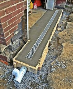 a drain pipe laying on the ground next to a brick wall and some concrete pipes