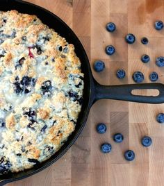 a skillet filled with blueberry cobbler on top of a wooden table next to fresh blueberries