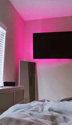 a bedroom with pink lighting and a flat screen tv mounted above the headboard, in front of a window