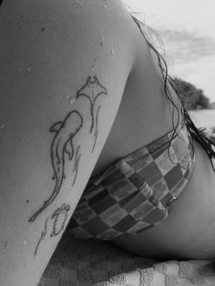 a woman laying on top of a beach next to the ocean with a tattoo on her arm