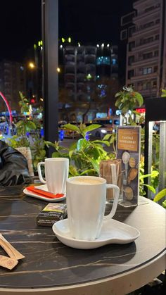 a table with two coffee cups and spoons on it, next to a book