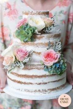 a woman holding a three tiered cake with succulents and flowers on it