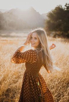 a woman standing in a field with her hands behind her head