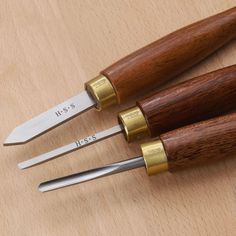 three knives are sitting next to each other on a wooden surface with gold trimmings