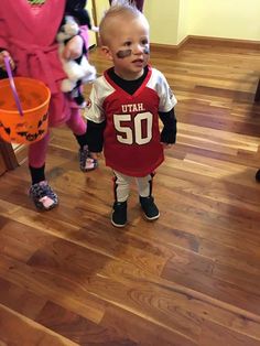 a little boy with his face painted in the shape of a football jersey standing next to two other children