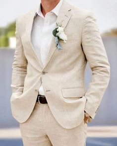 a man in a white suit and flower boutonniere stands with his hands in his pockets