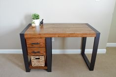 a wooden desk with two drawers and a basket under it on the floor next to a wall