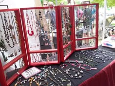 a table topped with lots of necklaces on display next to a red framed case