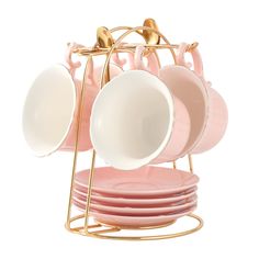 pink and white dishes are stacked on gold racks with matching saucers, plates and spoons