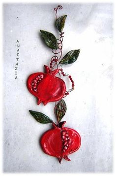 two red pomegranates with green leaves and beads hanging from the side