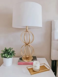 a white table with a lamp and some books on it next to a potted plant