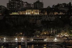 boats are docked in the water at night near a city with tall buildings and lit up lights