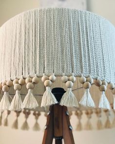 a white lamp with tassels on it and a wooden tripod light fixture