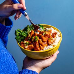 a person holding a yellow bowl filled with rice and broccoli covered in sauce