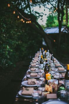 a long table is set up with plates and wine bottles for an outdoor dinner party