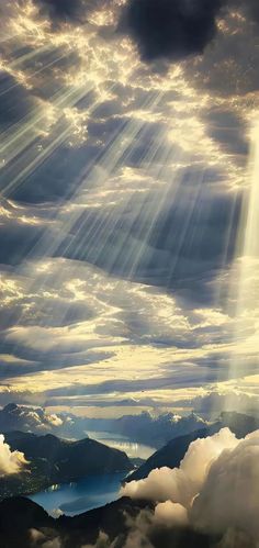 the sun shines through clouds over mountains and water in this artistic photo taken from an airplane